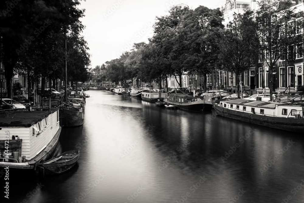Fototapeta premium Amsterdam, Holland, the Netherlands - July 6 2020: capture of the typical Amsterdam scenery in black and white with canal, canalo house, clouds and the iconic buildings of the city