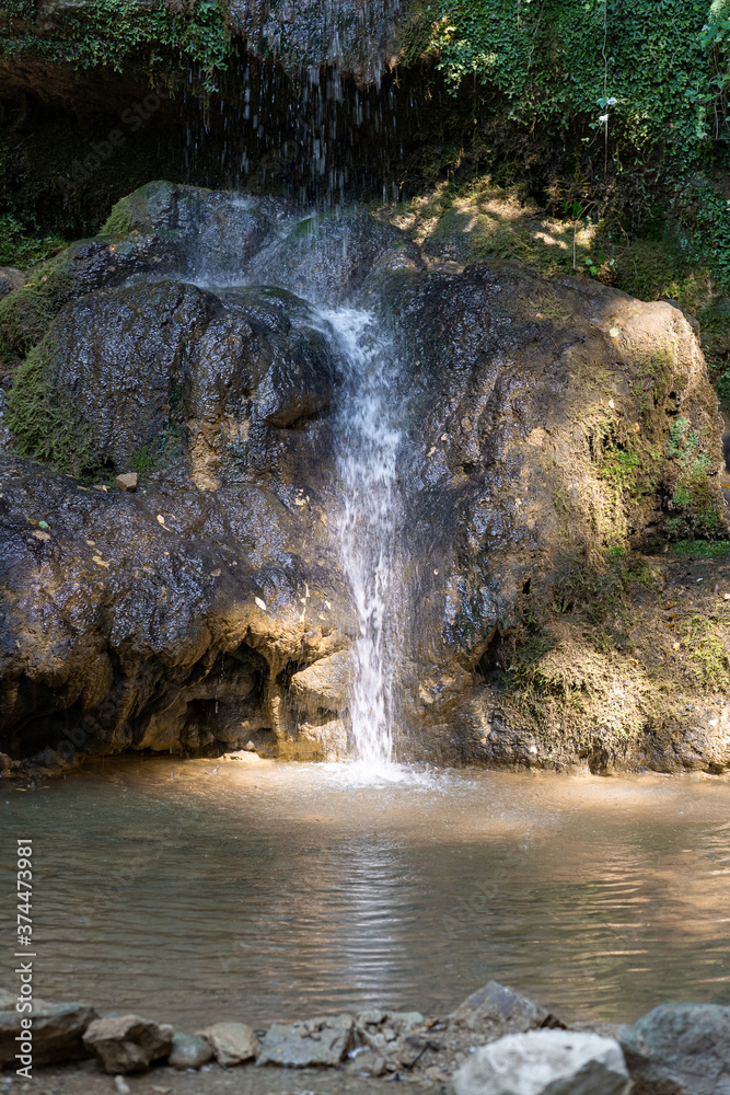 Fototapeta premium Small waterfall with reflecting lake and sunbeams in forest. Scenie for meditation concept. Biggest waterfall of canton Aargau, in Linner Bözberg, Switzerland.