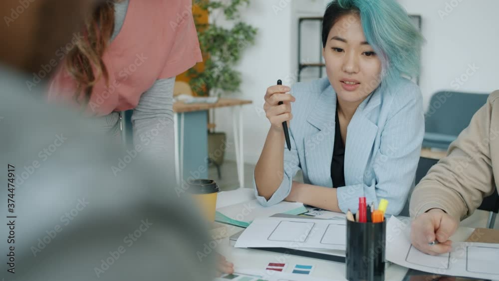 Asian young woman is talking to creative team of designers in workplace sharing business ideas looking at color samples. Youth and start-up concept. Asian young woman is talking to creative team of designers in workplace sharing business ideas looking at color samples. Youth and start-up concept.