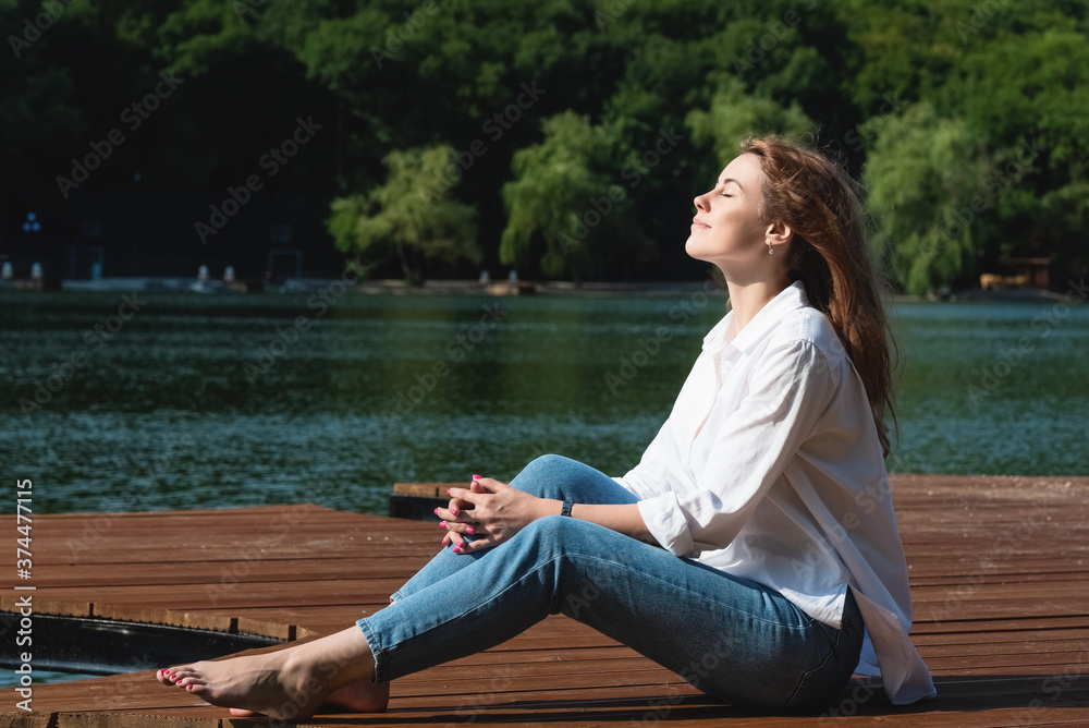 A beautiful and sexy woman, with long hair in a white shirt and jeans, spends time on the shore of the lake, surrounded by forests and mountains. Rest and relaxation concept A beautiful and sexy woman, with long hair in a white shirt and jeans, spends time on the shore of the lake, surrounded by forests and mountains. Rest and relaxation concept