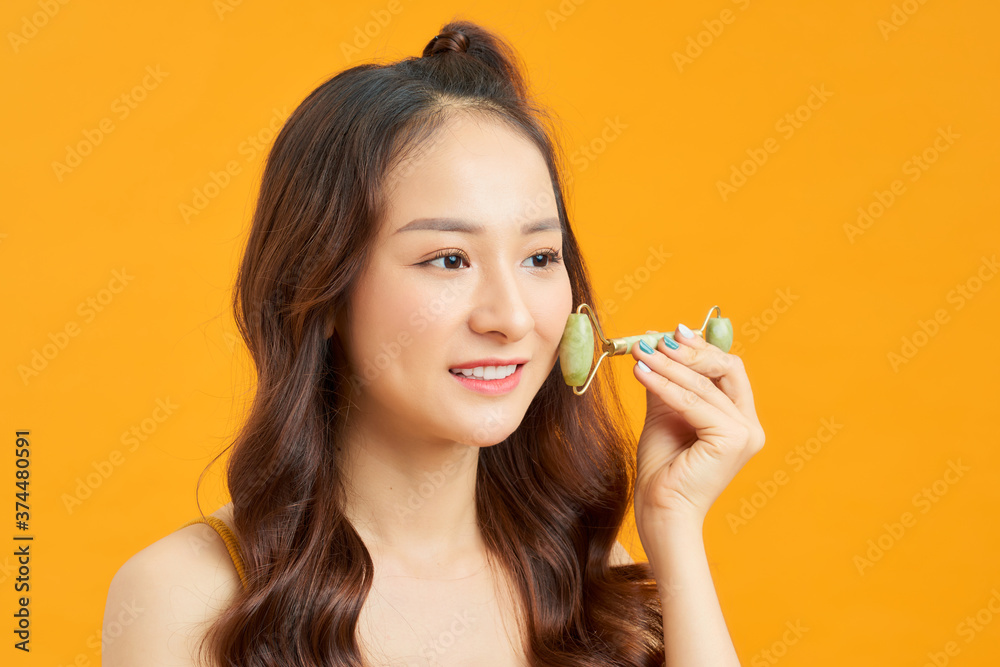 Beautiful Asian woman uses jade roller to massage her face Beautiful Asian woman uses jade roller to massage her face