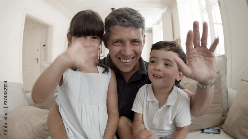 Happy dad and two cute kids smiling and waving hello at webcam, having video call. Father hugging children. Pov shot, fisheye. Communication concept Happy dad and two cute kids smiling and waving hello at webcam, having video call. Father hugging children. Pov shot, fisheye. Communication concept