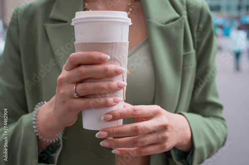young brunette woman in a green jacket on a walk. Beautiful girl with takeaway coffee with hands