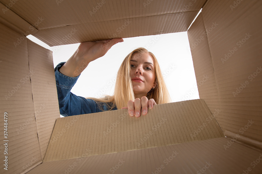 © Plutmaverick - Young beautiful girl blonde, opens and peeks into a cardboard box. To get or to put things to move, bottom view.