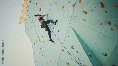 Young woman climbing up, then coming down from rocky wall indoors, below view