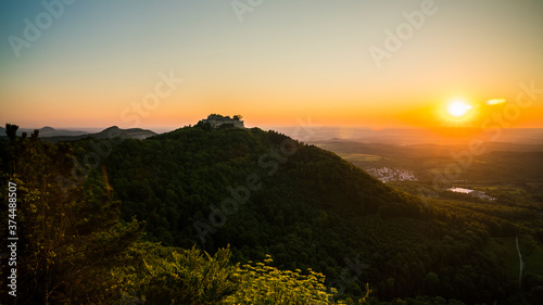 Germany, Aerial scenic view above green valleys of swabian alb nature landscape and castle ruins of hohenneuffen on mountain in warm orange sunset light