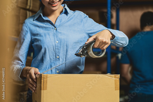 Obraz na płótnie Closeup of Warehouse worker woman packing cardboard box with sticky tape with Indian worker man in local warehouse or factory, industry and export business concept, partner and colleague work together w salonie