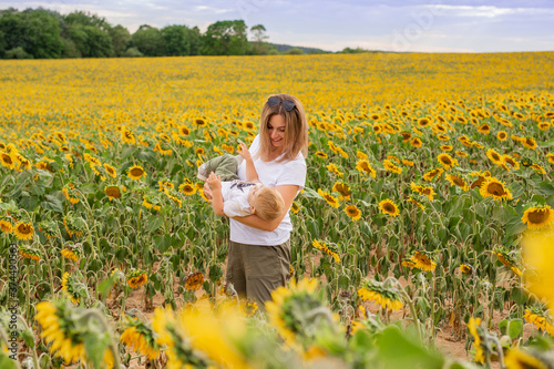 little boy with mom in a white t-shirt walks in a field of sunflowers	