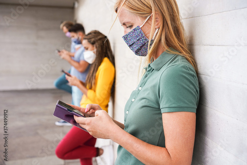 Young people wearing face safety masks using mobile phones while keeping social distance during coronavirus outbreak - Technology and covid-19 spread prevention concept - Focus on right woman eye
