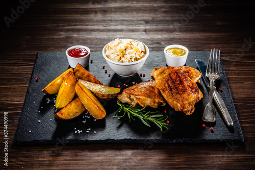Foto Barbecue chicken thighs with fried potatoes and coleslaw on stone plate