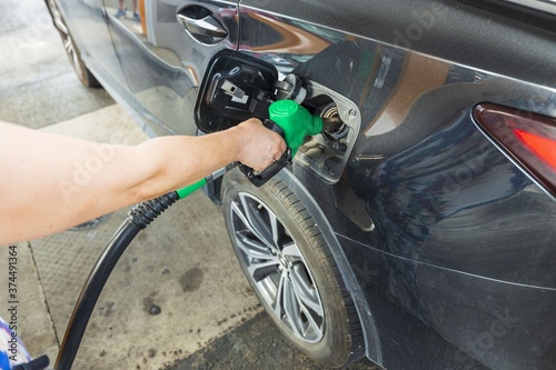 Woman pours fuel into the tank of a black car on gasoline station. Transportation concept. Beautiful backgrounds.