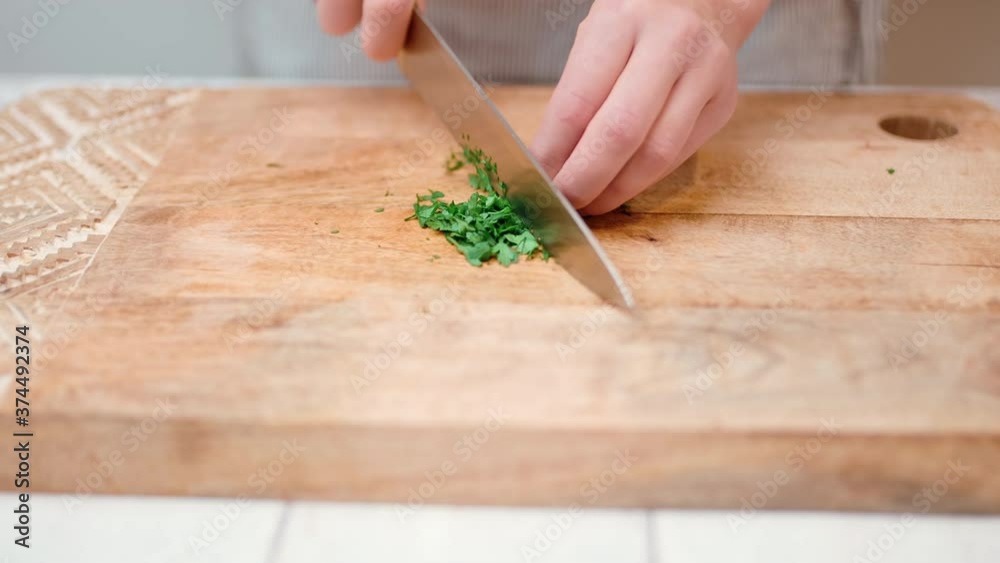 Close-up chopping parsley/greens with a chef knife in 4K. Concept of cutting/slicing parsley/greens on a cutting board in slow motion.