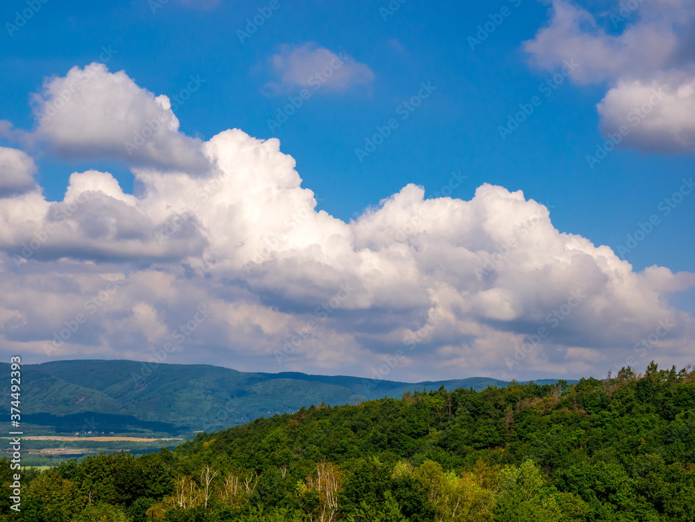 Massive clouds - towering cumulus - forming in the blue sky over hilly landscape Massive clouds - towering cumulus - forming in the blue sky over hilly landscape