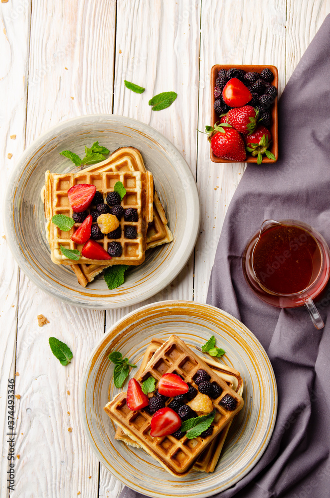 Flat view at belgian waffles served with strawberries and blackberries on white wooden kitchen table closeup Flat view at belgian waffles served with strawberries and blackberries on white wooden kitchen table closeup
