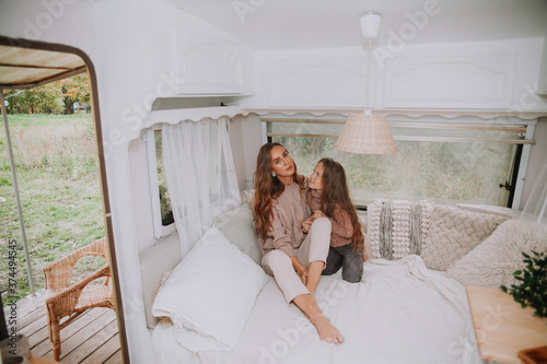 Happy family - mother and little daughter relaxing hugging and having fun in countryside inside white scandinavian rustic camper van interior. Domestic tourism concept.