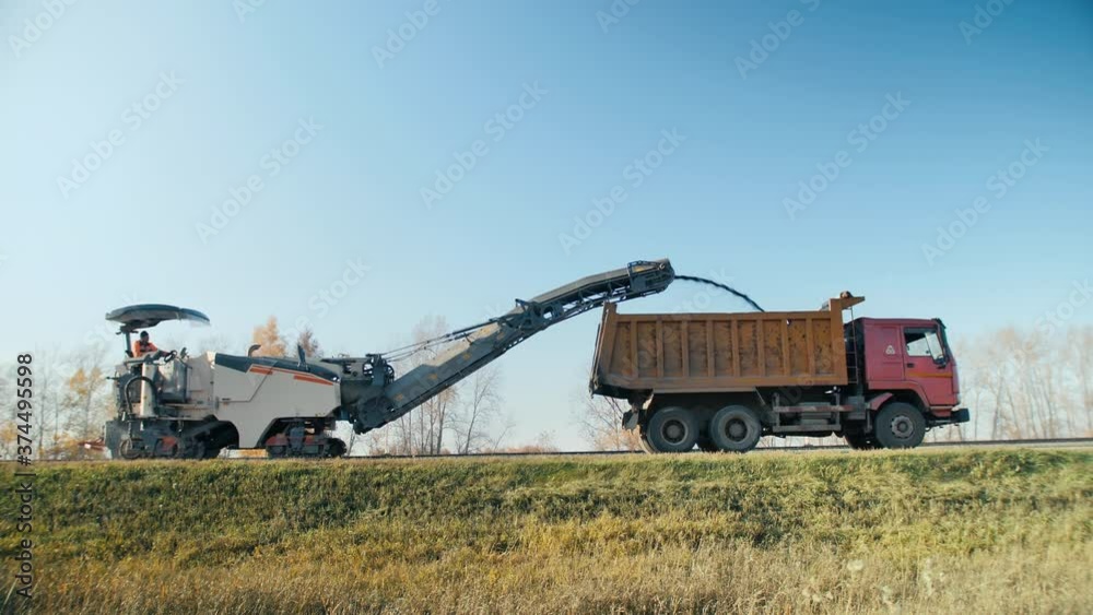 Roadworks. Asphalt the road. Removing the old layer of asphalt with a milling and grinding machine. Road construction works. An asphalt paver pours powdered asphalt into a truck. Roadworks. Asphalt the road. Removing the old layer of asphalt with a milling and grinding machine. Road construction works. An asphalt paver pours powdered asphalt into a truck.