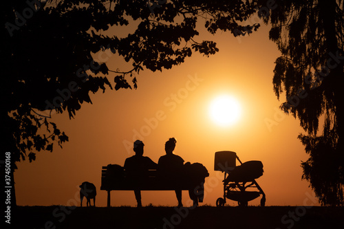 silhouette of a couple sitting on a bench at sunset or sunrise with a stroller and a dog