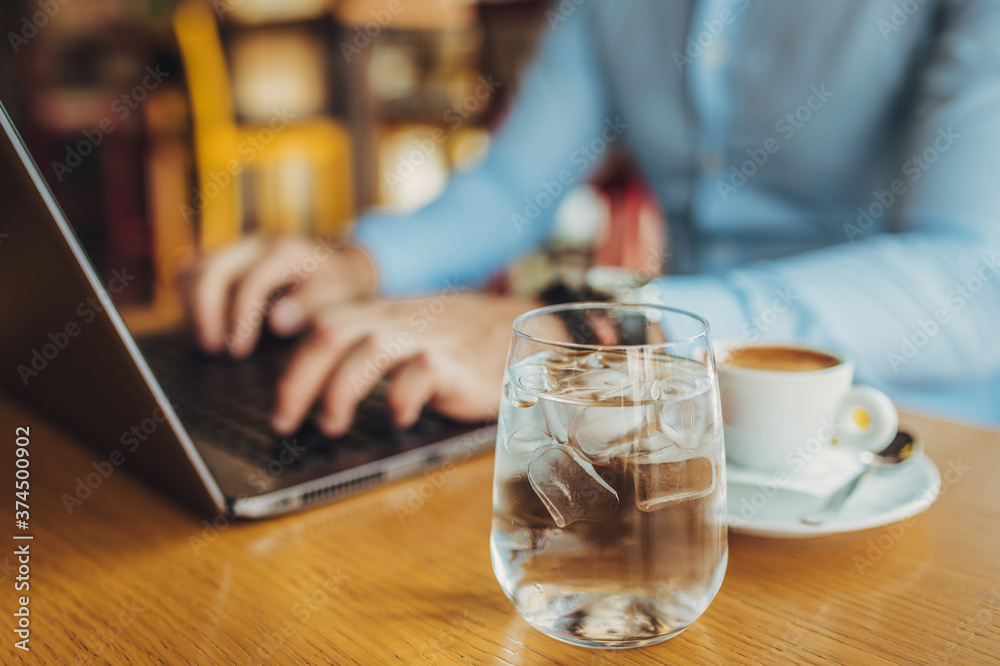 Close up of a business man enjoying coffee in a Cafe and using a laptop.a glass of water in focus