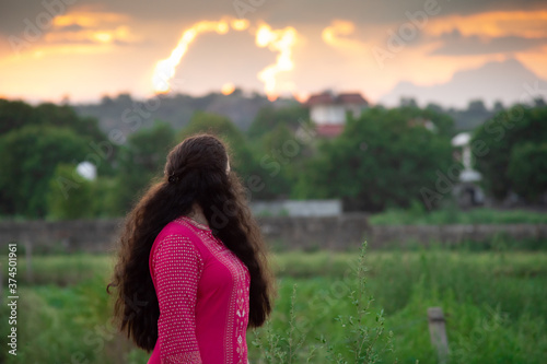 Young Indian girl wearing a mask, indian salwar kameez standing with a field and a beautiful sunset behind her photo