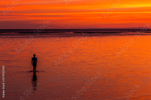 Silhouette of a man walking in the ocean at sunset