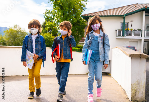 Three brothers with face masks ready to go back to school. New normality, social distance, coronavirus pandemic, covid-19. Leaving home with all security measures © unai