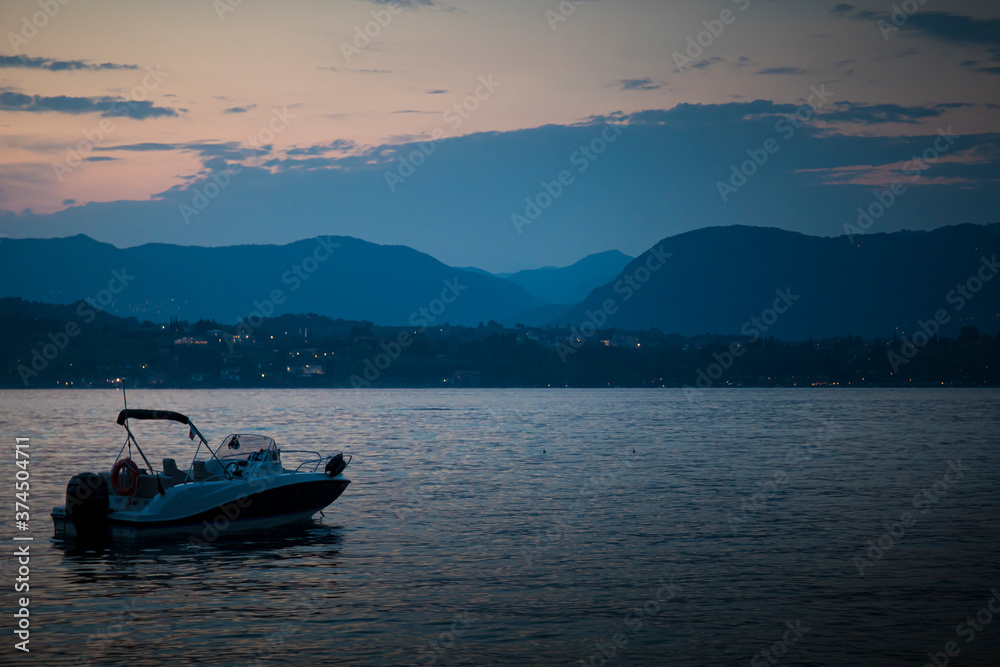Garda Lake dusk, blue hour landscape, with a still speedboat and the hills in the background. Manerba del Garda, Lombardy, Italy.