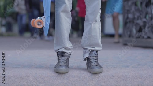 A man stands on the road and holds a skate in his hands. People are walking around