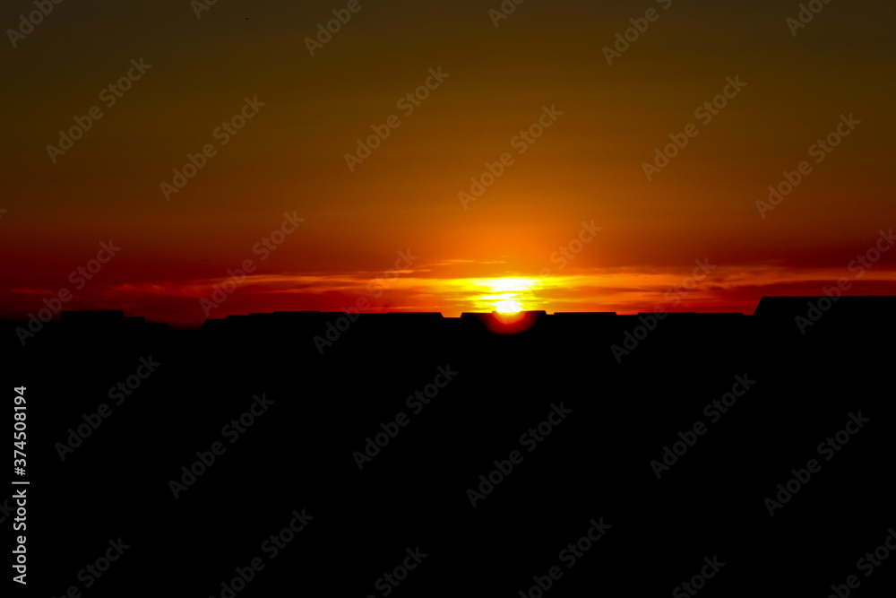 Full orange sky during sunset and silhouette houses