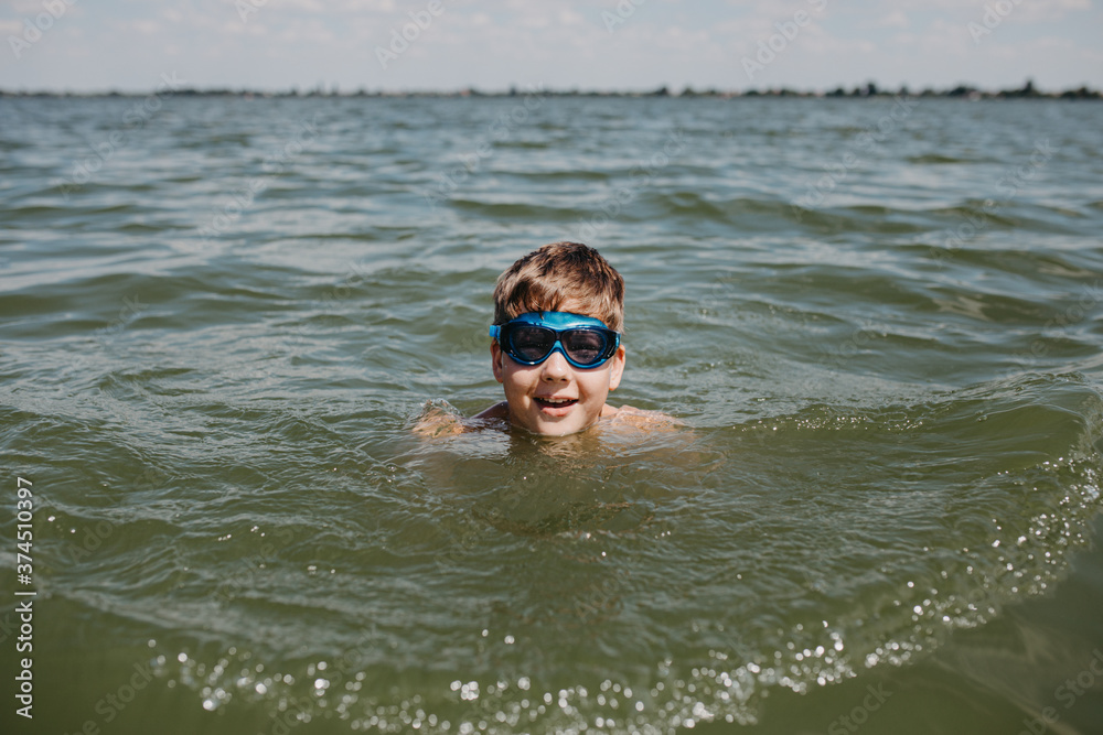 Teenager boy wearing goggles swimming in a lake. Summer vacation time