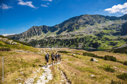 Fototapeta Naklejka Na Ścianę i Meble -  Group of hikers walks through the valley in the High Mountains. Alpine style landscape in the summer. Tourism in outdoors. Beautifull landscape in Poland.	