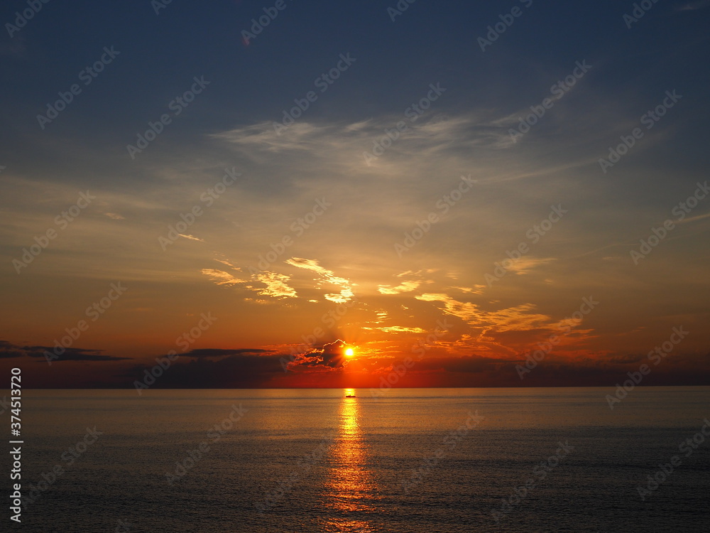 Naklejka premium sunrise through clouds with passing boat