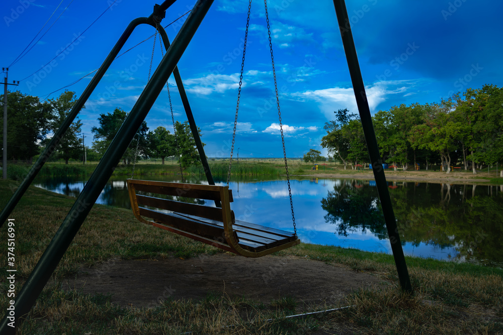 Swing for relaxation in an empty evening park by the lake at sunset