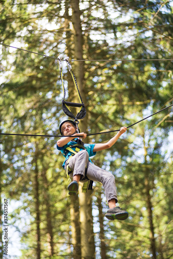 A boy pulls himself up by a rope in a high rope park