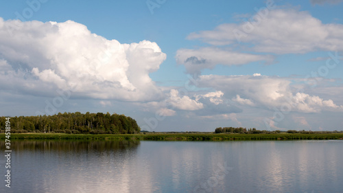 Forest lake view, smooth surface of a lake with clouds reflected, shining level of a forest lake