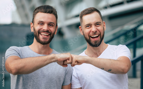 Obraz na plátně Two happy excited modern bearded best friends in casual clothes having fun and chatting together outdoors