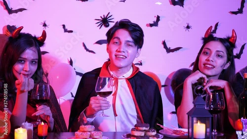 Group of young asian,2 wowan and 1 man in Halloween costume, beckoning, behind foreground of counter bar decorated with candles, snacks and wine glass. Indoor Halloween Night Party Concept photo