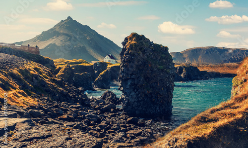 Famous Icelandic view. basalt rocks formation on coastline with beautiful hous and Mountain Stapafell in the background at Arnarstapi Village in summer sunny day in Iceland. Amazing nature of Iceland photo