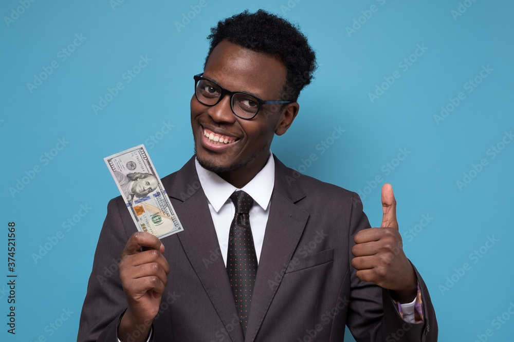 African man in suit holding dollars with big smile doing thumb up with finger. African man in suit holding dollars with big smile doing thumb up with finger.