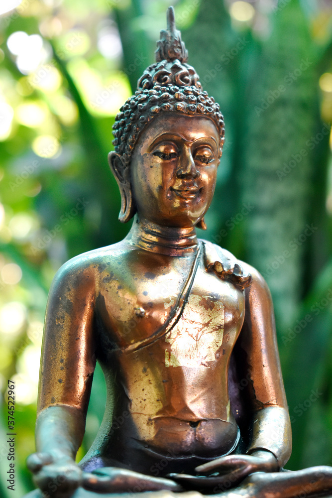 The brass Buddha sitting on the brass seat has a respectable beauty, on a blurred background.