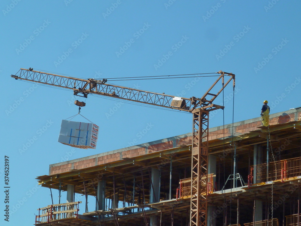 Novi Sad, Serbia, August 29th 2014. - A worker standing on the building construction controls the lifting of the load crane