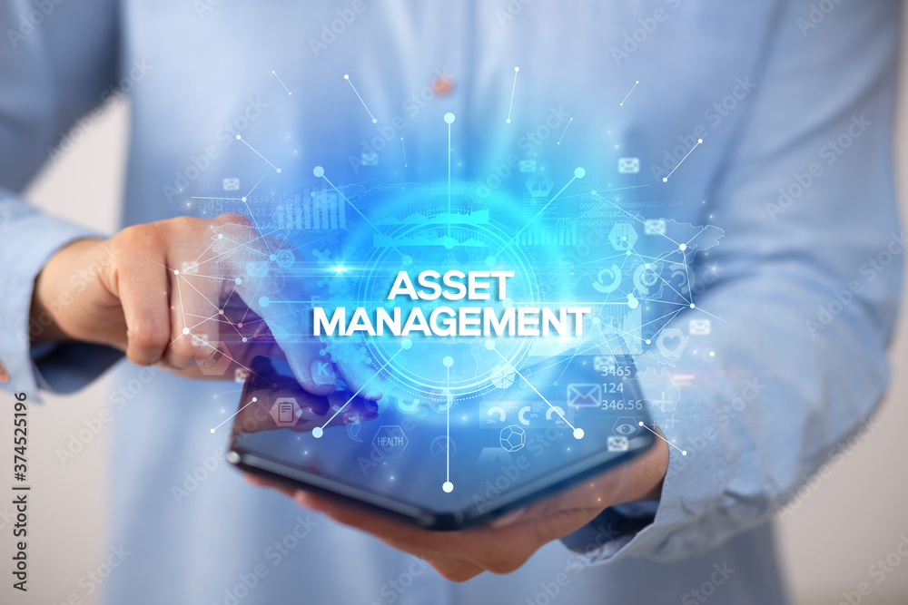 Businessman holding a foldable smartphone with ASSET MANAGEMENT inscription, new business concept Businessman holding a foldable smartphone with ASSET MANAGEMENT inscription, new business concept