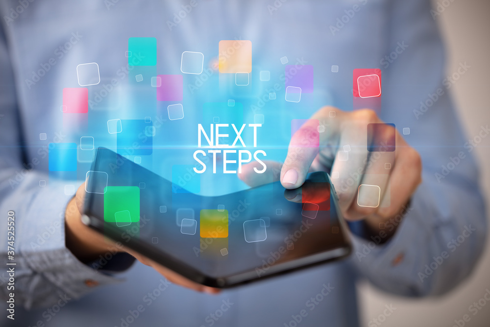 Young man holding a foldable smartphone with NEXT STEPS inscription, educational concept Young man holding a foldable smartphone with NEXT STEPS inscription, educational concept
