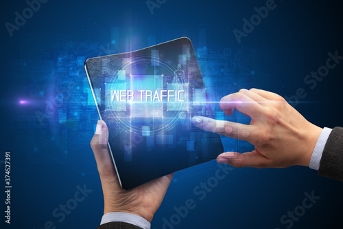 Businessman holding a foldable smartphone with WEB TRAFFIC inscription, new technology concept