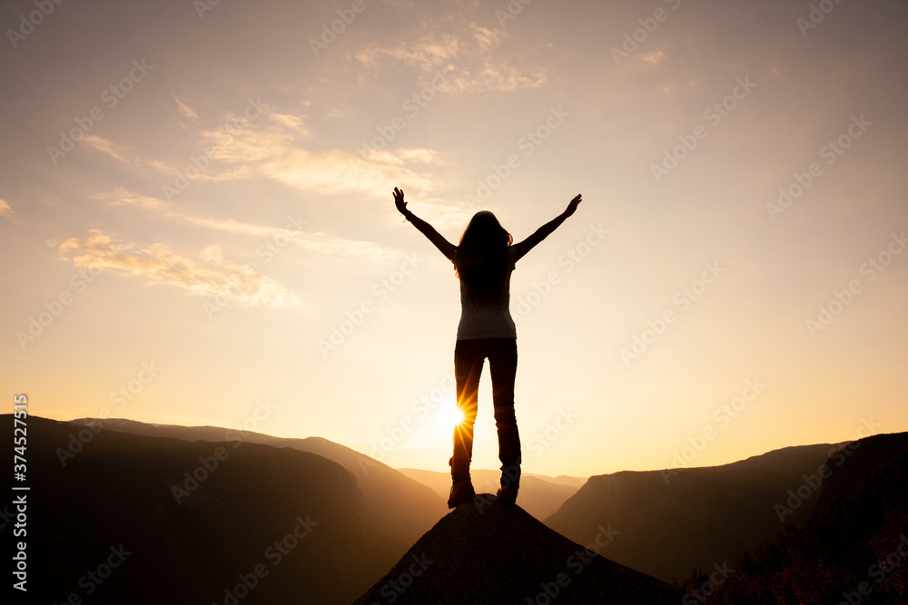 Silhouette einer Frau mit ausgebreiteten Armen bei Sonnenaufgang  auf einem Berggipfel