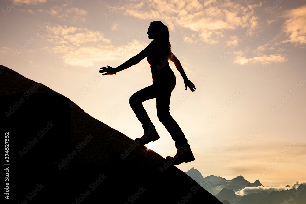 Silhouette einer Frau beim Aufstieg  auf einen Berggipfel bei Sonnenaufgang