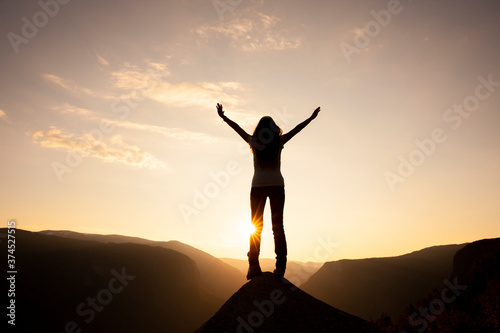 Silhouette einer Frau mit ausgebreiteten Armen bei Sonnenaufgang auf einem Berggipfel