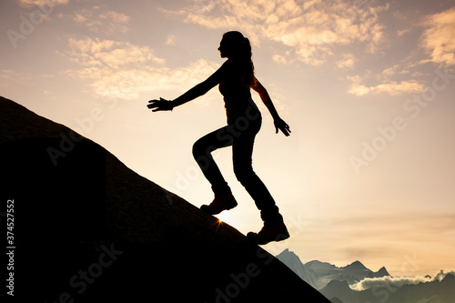 Silhouette einer Frau beim Aufstieg  auf einen Berggipfel bei Sonnenaufgang