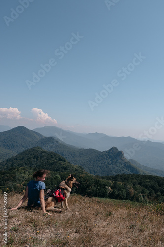 Dog traveler goes to the mountains with his best friend man and enjoys nature and beautiful scenery. A young traveller girl is sitting on top of a mountain with her German shepherd.