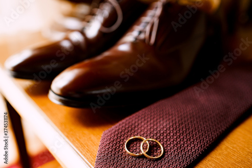 Wedding gold rings for the bride and groom on a tie with brown shoes on a wooden table.