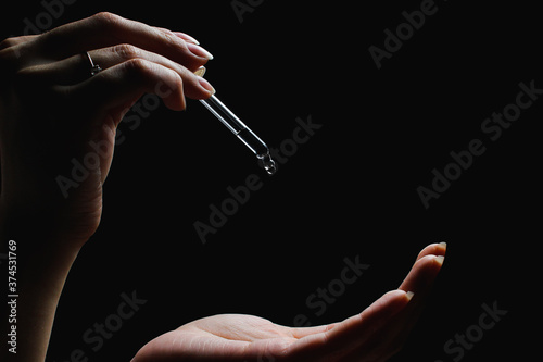 female with beautiful nails hold pipette over another hand, isolated on black background

D